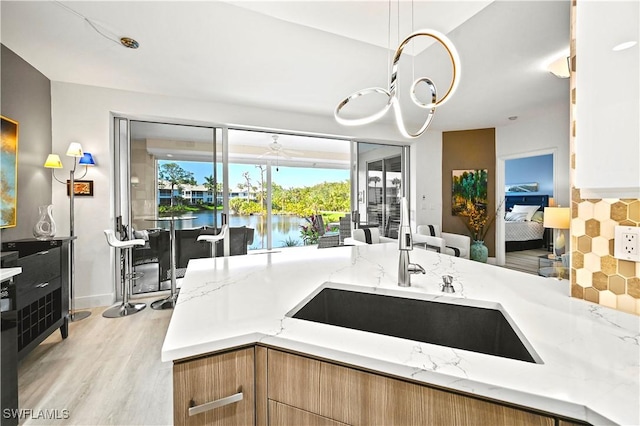 kitchen featuring light stone counters, light wood-style flooring, a sink, hanging light fixtures, and backsplash