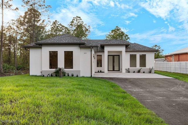 view of front of home with a shingled roof, fence, french doors, a front yard, and stucco siding