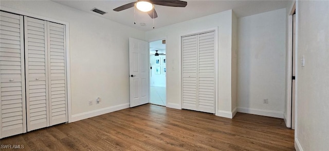 unfurnished bedroom featuring multiple closets, wood finished floors, visible vents, and baseboards