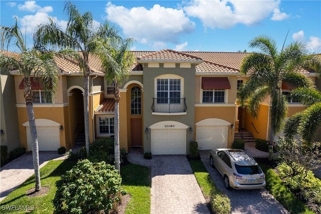 mediterranean / spanish-style house with a garage, a tiled roof, decorative driveway, and stucco siding