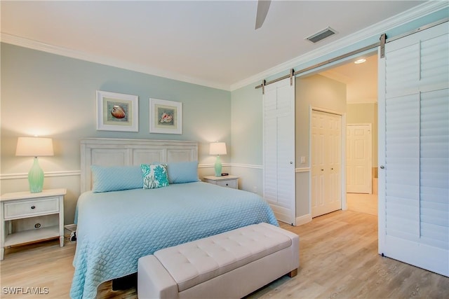 bedroom featuring ornamental molding, a barn door, light wood-style flooring, and visible vents