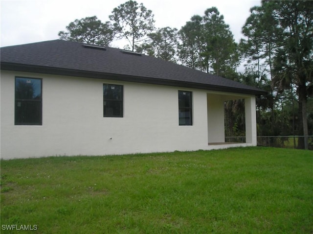 back of property with roof with shingles, a lawn, fence, and stucco siding