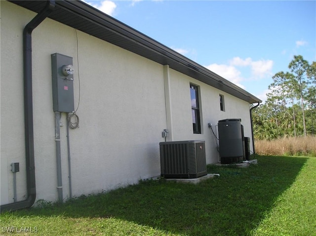 view of side of property featuring stucco siding, cooling unit, and a yard