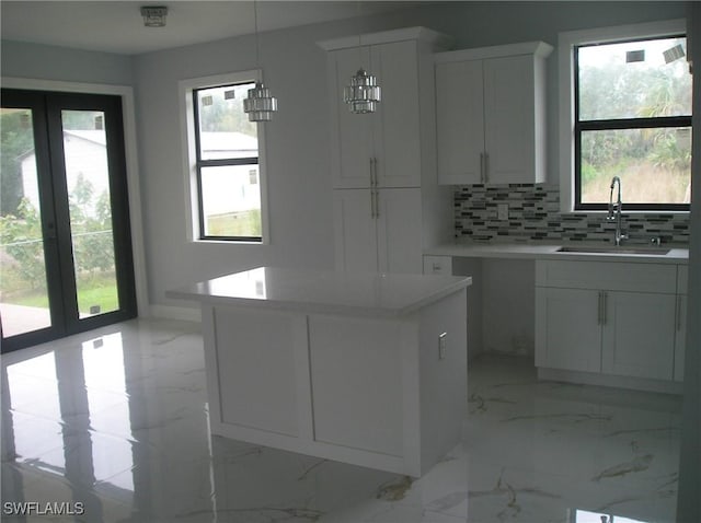 kitchen with decorative backsplash, a kitchen island, marble finish floor, white cabinetry, and a sink