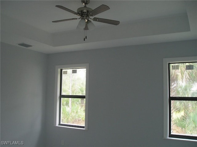 spare room with a raised ceiling, visible vents, and a ceiling fan