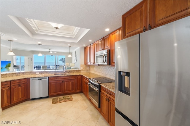 kitchen with stainless steel appliances, a tray ceiling, a sink, and brown cabinets