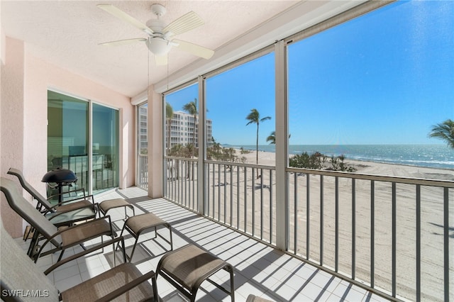 sunroom with a beach view, a ceiling fan, and a water view