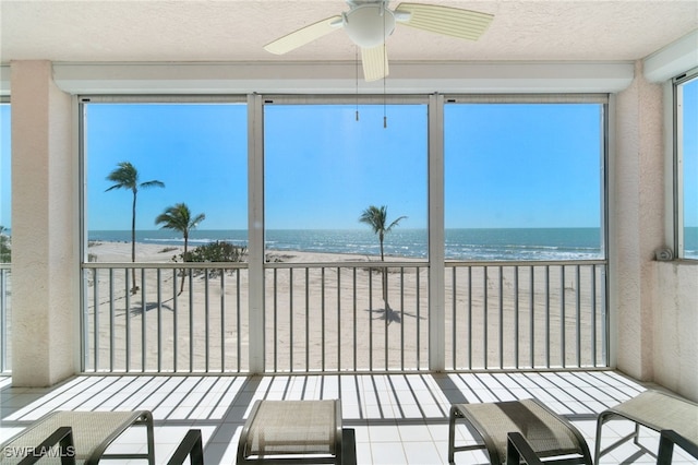 sunroom / solarium featuring a water view, a beach view, and a ceiling fan