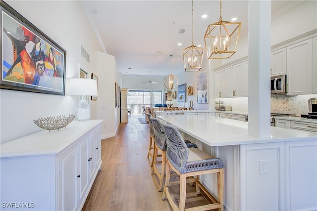 kitchen featuring visible vents, white cabinets, light countertops, decorative backsplash, and stainless steel microwave