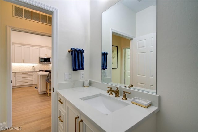 bathroom with tasteful backsplash, visible vents, vanity, and wood finished floors