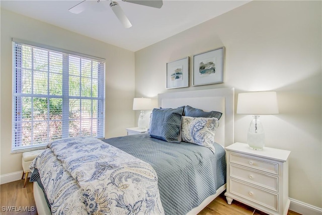 bedroom featuring ceiling fan, multiple windows, baseboards, and wood finished floors