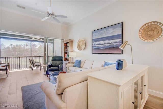 living room with light wood finished floors, visible vents, baseboards, a ceiling fan, and crown molding