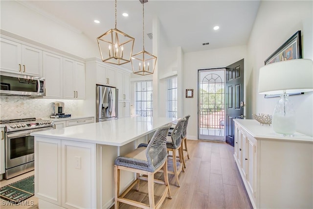 kitchen featuring a breakfast bar area, white cabinetry, appliances with stainless steel finishes, a center island, and light wood finished floors