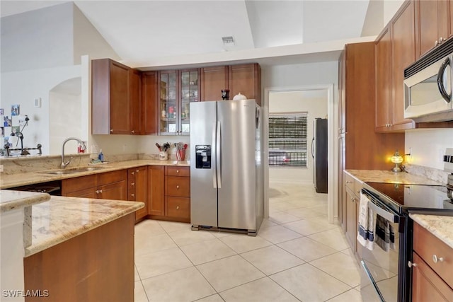kitchen featuring light stone countertops, a sink, vaulted ceiling, appliances with stainless steel finishes, and brown cabinets