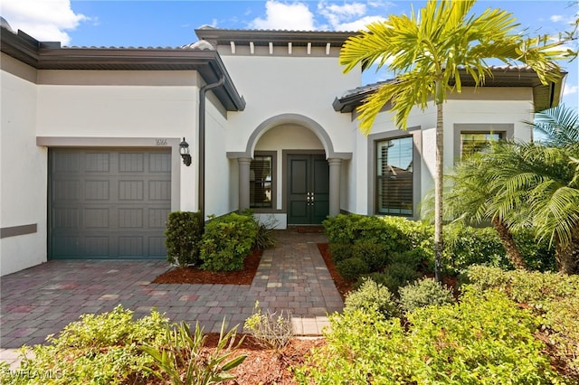 property entrance with decorative driveway, an attached garage, and stucco siding