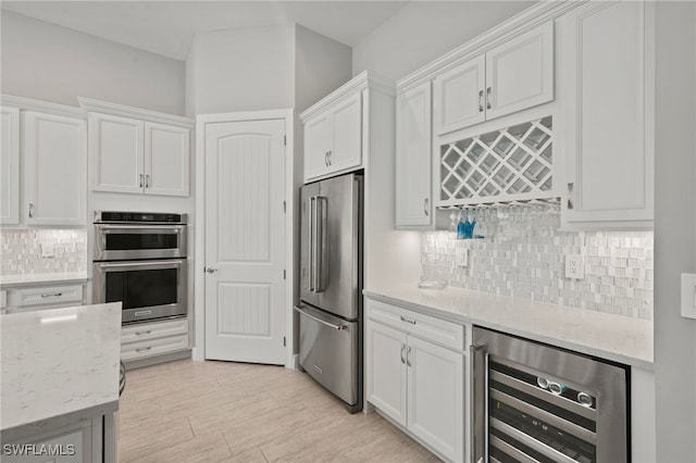 kitchen featuring white cabinetry, beverage cooler, light stone countertops, and stainless steel appliances