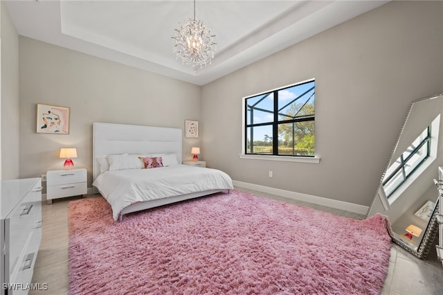 bedroom featuring an inviting chandelier, a raised ceiling, and baseboards