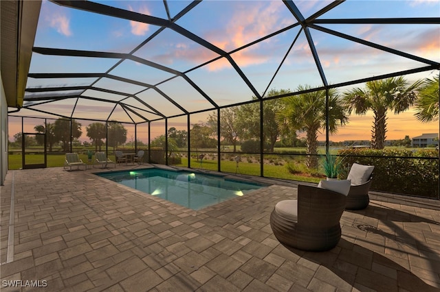 pool at dusk featuring an outdoor pool, a patio, and a lanai