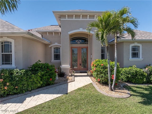 property entrance featuring stucco siding, a shingled roof, a lawn, and french doors