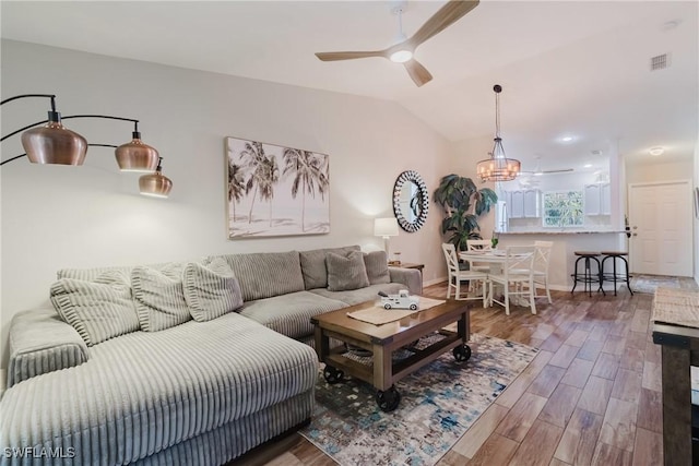 living area with vaulted ceiling, ceiling fan with notable chandelier, baseboards, visible vents, and wood finished floors
