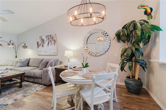 dining area featuring an inviting chandelier, baseboards, vaulted ceiling, and wood finished floors