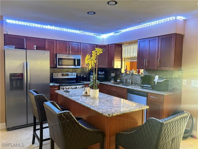 kitchen featuring light tile patterned floors, a sink, appliances with stainless steel finishes, reddish brown cabinets, and tasteful backsplash