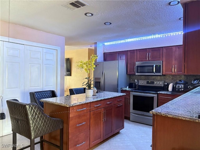 kitchen with visible vents, appliances with stainless steel finishes, a breakfast bar, dark brown cabinets, and backsplash