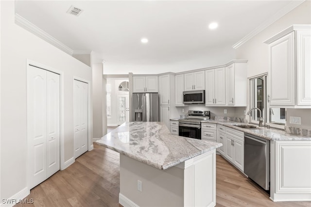 kitchen with stainless steel appliances, a sink, ornamental molding, a center island, and light wood finished floors