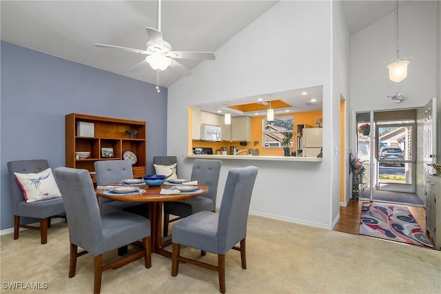 dining area with a ceiling fan, light colored carpet, baseboards, and high vaulted ceiling