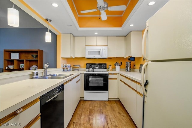 kitchen featuring light wood-style flooring, a sink, a tray ceiling, white appliances, and light countertops