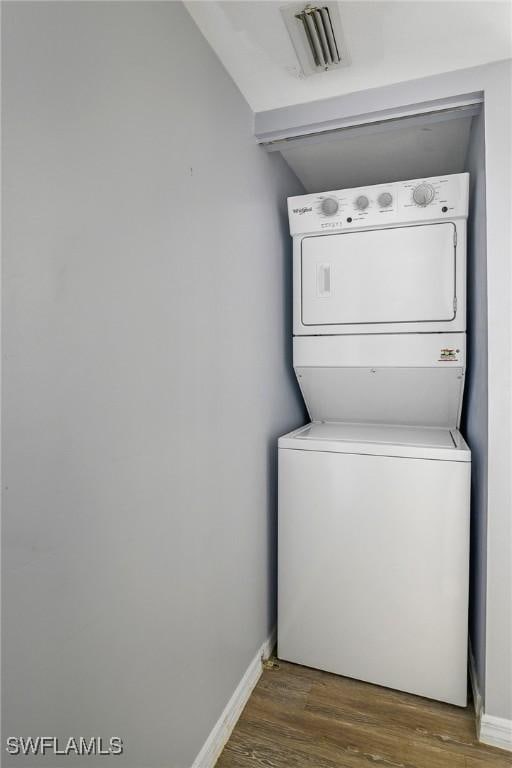 laundry room featuring visible vents, baseboards, laundry area, wood finished floors, and stacked washer / drying machine