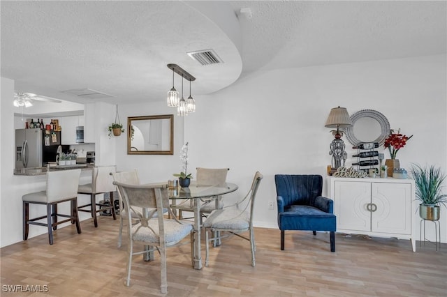 dining space featuring light wood-type flooring, a ceiling fan, visible vents, and a textured ceiling