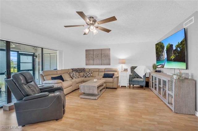 living room with light wood-type flooring, ceiling fan, visible vents, and a textured ceiling