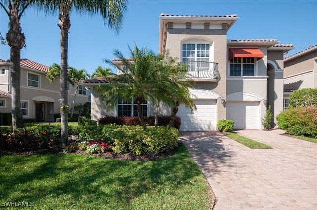 mediterranean / spanish-style home featuring an attached garage, a balcony, decorative driveway, stucco siding, and a front yard