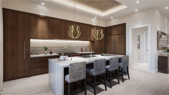 kitchen with a center island with sink, a sink, tasteful backsplash, modern cabinets, and light wood-type flooring