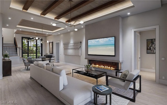 living room featuring baseboards, beam ceiling, light wood-style flooring, a glass covered fireplace, and a raised ceiling