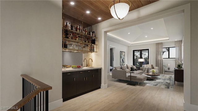 bar featuring a raised ceiling, a sink, recessed lighting, light wood finished floors, and wet bar