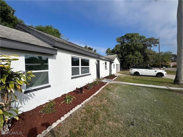 view of side of home featuring roof with shingles, a lawn, and stucco siding