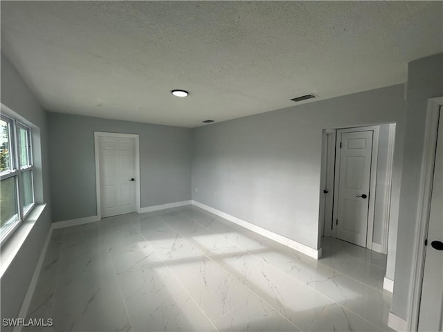 spare room featuring marble finish floor, visible vents, baseboards, and a textured ceiling