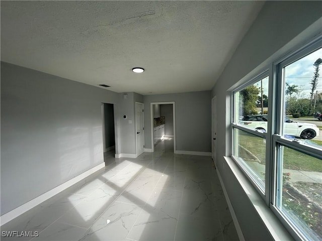 unfurnished room featuring a textured ceiling, marble finish floor, visible vents, and baseboards