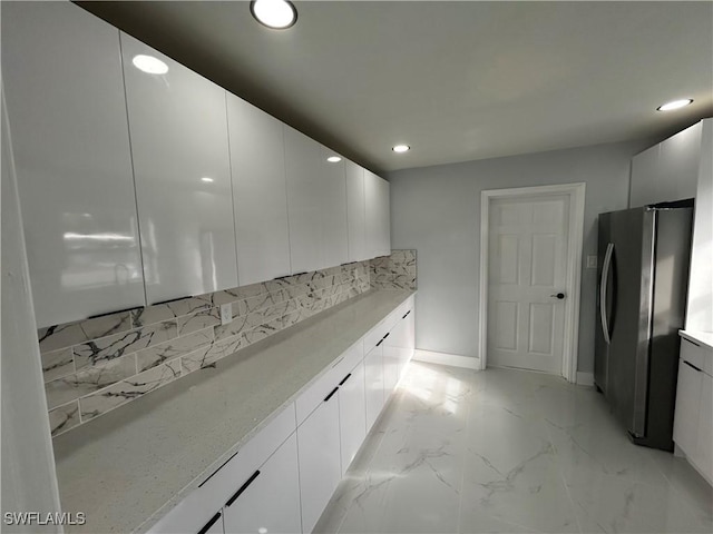 kitchen featuring decorative backsplash, modern cabinets, freestanding refrigerator, marble finish floor, and white cabinetry