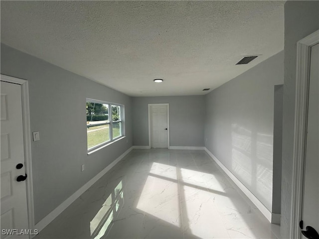 unfurnished room featuring marble finish floor, baseboards, visible vents, and a textured ceiling