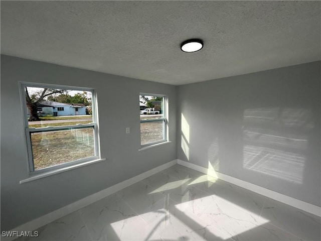 spare room with a textured ceiling, marble finish floor, and baseboards