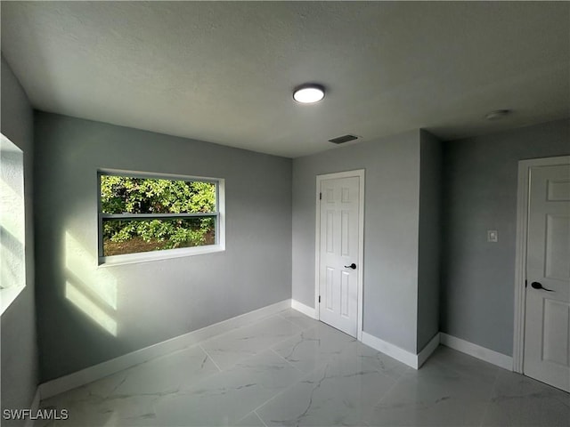 empty room featuring marble finish floor, visible vents, a textured ceiling, and baseboards