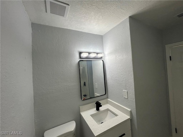 half bath with visible vents, a textured wall, toilet, vanity, and a textured ceiling