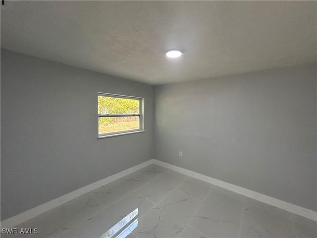 spare room featuring a textured ceiling, marble finish floor, and baseboards