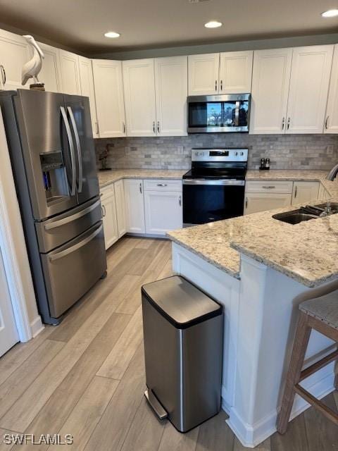 kitchen with light wood finished floors, white cabinets, appliances with stainless steel finishes, a kitchen breakfast bar, and light stone countertops