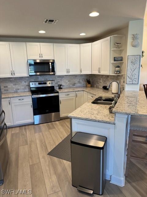 kitchen featuring appliances with stainless steel finishes, a peninsula, white cabinetry, open shelves, and a sink