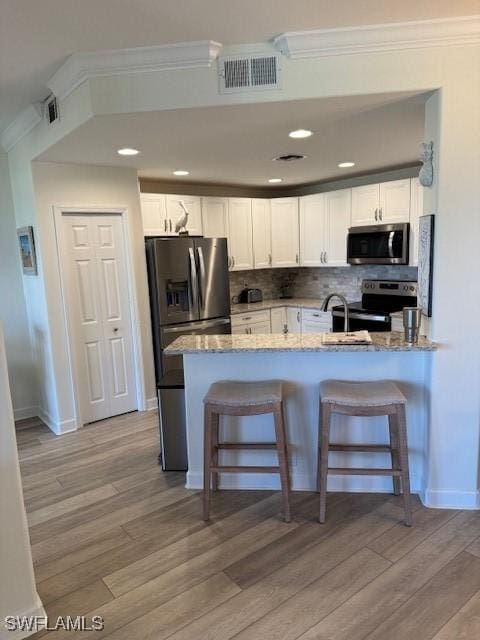 kitchen featuring a peninsula, appliances with stainless steel finishes, visible vents, and white cabinets