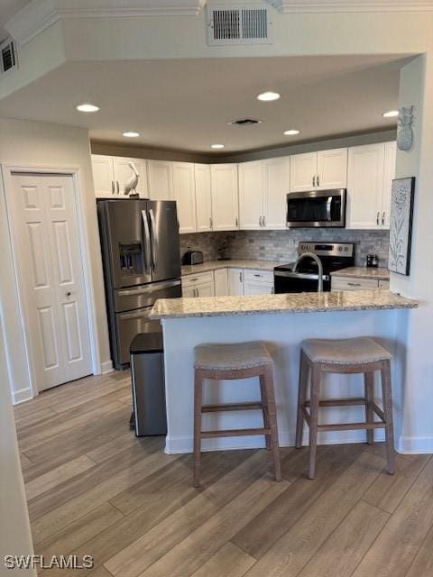 kitchen featuring visible vents, white cabinets, a peninsula, light stone countertops, and stainless steel appliances